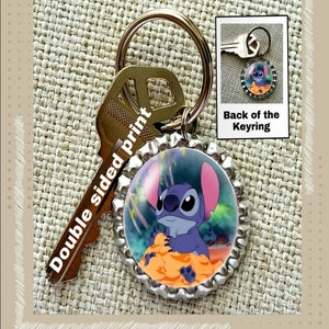 May include: A blue Stitch character keychain made from a bottle cap. The keychain is double-sided and features a key ring. The back of the keychain shows a plain blue bottle cap.