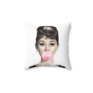 May include: A white square pillow with a black and white image of a woman blowing a pink bubble. The woman is wearing a black dress and a pearl necklace.