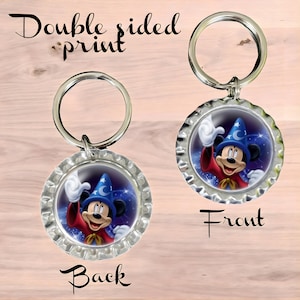 May include: Double-sided keychain featuring a cartoon image of Mickey Mouse dressed as a sorcerer. The front side shows Mickey Mouse with his hand raised, wearing a blue sorcerer's hat with a crescent moon and star. The background is a dark blue with white stars. The back side shows the same image but flipped horizontally. The keychain is made of metal and has a silver finish.