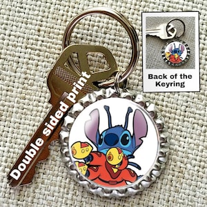 May include: A blue Stitch character from Lilo & Stitch is printed on a silver bottle cap keychain. The keychain is attached to a gold key ring and a silver key. The back of the keychain shows a different image of Stitch.