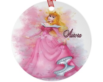 Könnte beinhalten: Ein rosa-weißer Weihnachtsbaumschmuck im Aquarellstil mit einem Cartoon-Bild von Prinzessin Aurora aus Dornröschen. Der Schmuck hat ein rotes Band und der Text "Aurora" ist auf der rechten Seite des Schmucks gedruckt.