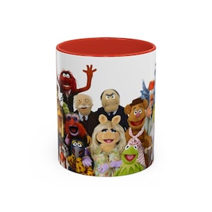 Peut inclure: Une tasse en céramique blanche avec un bord rouge représentant une image colorée des personnages des Muppets. Les personnages incluent Miss Piggy, Kermit la grenouille, Fozzie Bear, Animal, et plus encore.