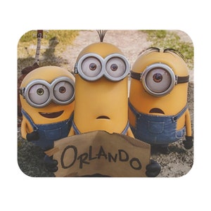 May include: Three yellow Minions with blue overalls and goggles are holding a cardboard sign that says "ORLANDO".