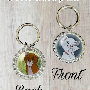 May include: Double-sided keychain featuring a cartoon cat on one side and a cartoon cat on the other side. The keychain is made of metal and has a silver finish. The text "Front" and "Back" is printed below the keychains.