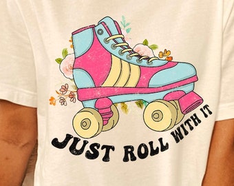 May include: White t-shirt with a graphic of a pink and blue roller skate with yellow accents and flowers. The text "Just Roll With It" is printed below the roller skate.