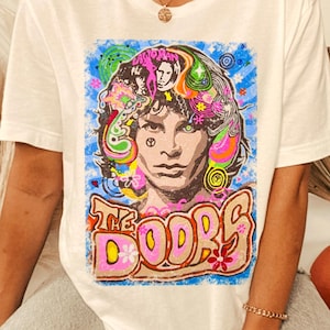 May include: White t-shirt with a colorful graphic print of Jim Morrison, the lead singer of The Doors. The graphic features a psychedelic design with flowers, swirls, and the band's name.