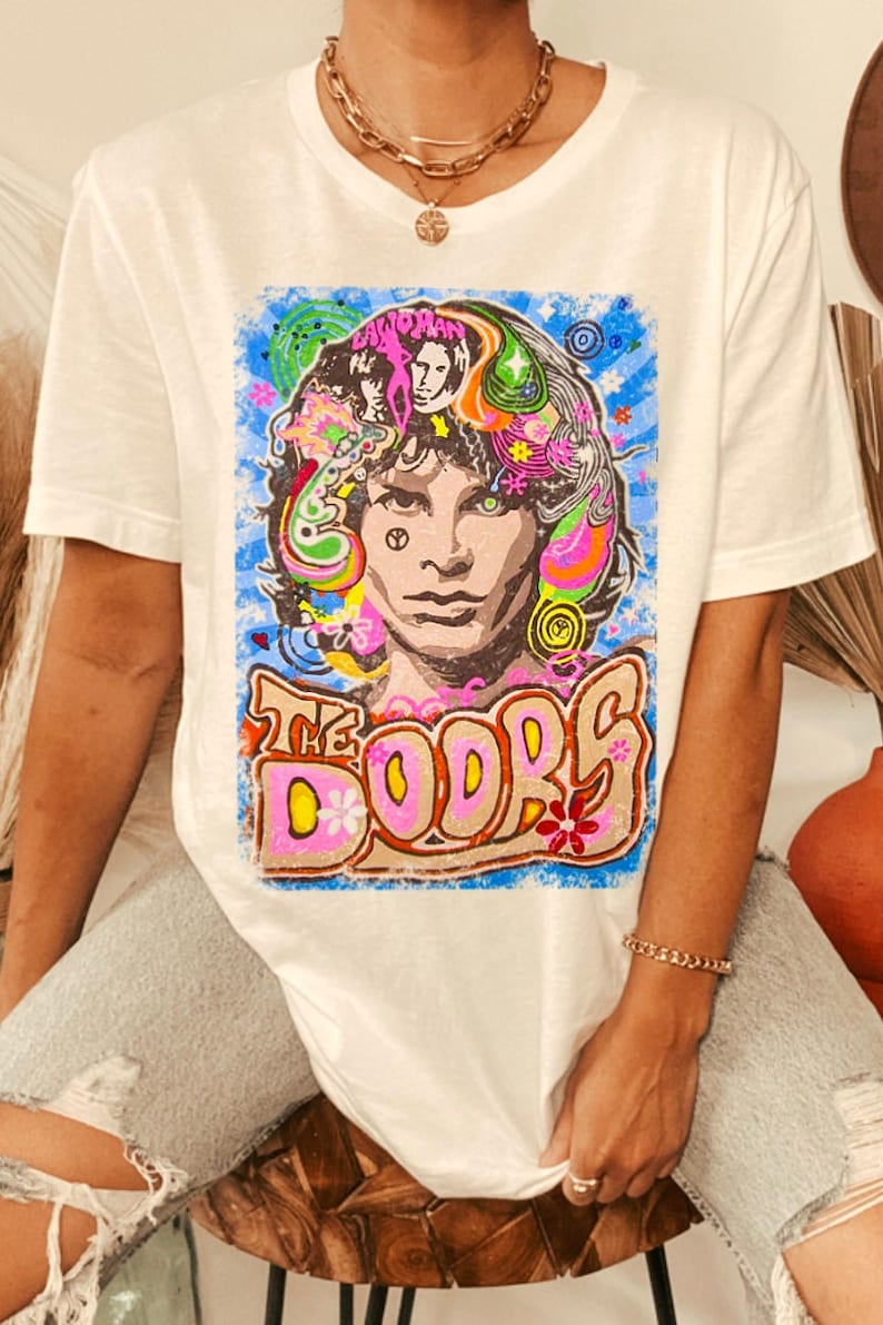 May include: White t-shirt with a colorful graphic print of Jim Morrison, the lead singer of The Doors. The graphic features a psychedelic design with flowers, swirls, and the band's name.