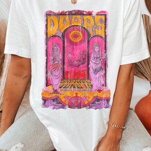 May include: White t-shirt with a vintage graphic print of a band called "Doors" with the text "Sat. Nite June 15" and other details. The graphic is in pink, yellow, and orange.
