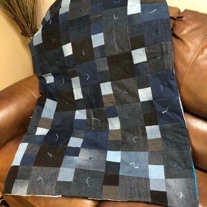 Könnte beinhalten: Eine Patchwork-Decke aus Jeansstoff in Blautönen und Schwarz. Die Decke besteht aus Quadraten unterschiedlicher Größe und ist mit einem kontrastierenden Faden zusammengenäht.