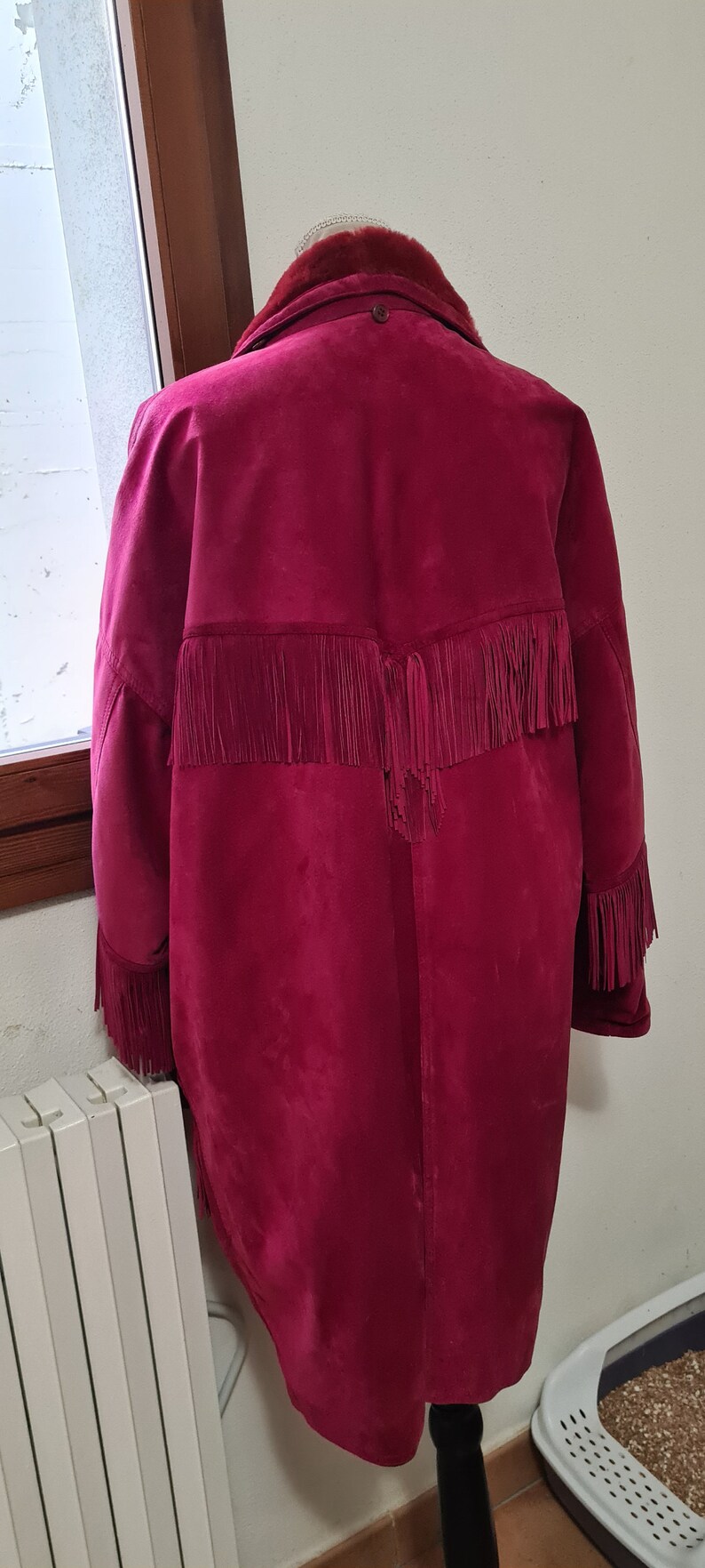 May include: A burgundy suede jacket with fringe detailing on the back and sleeves. The jacket has a fur collar.