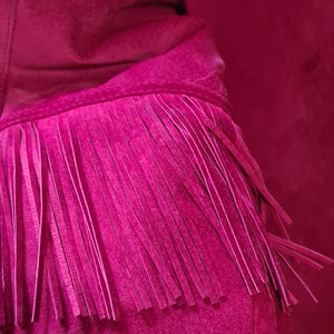 May include: A close-up of a magenta suede jacket with fringe detailing on the sleeves and hem.