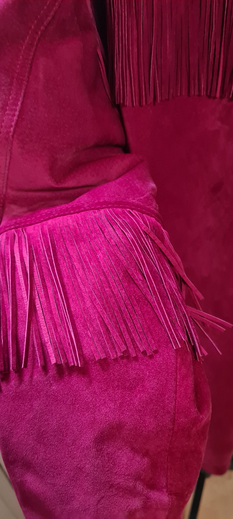 May include: A close-up of a magenta suede jacket with fringe detailing on the sleeves and hem.