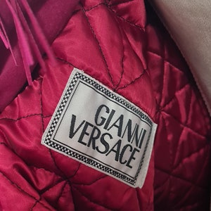May include: A close-up of the inside of a pink jacket with a white label that reads "Gianni Versace".