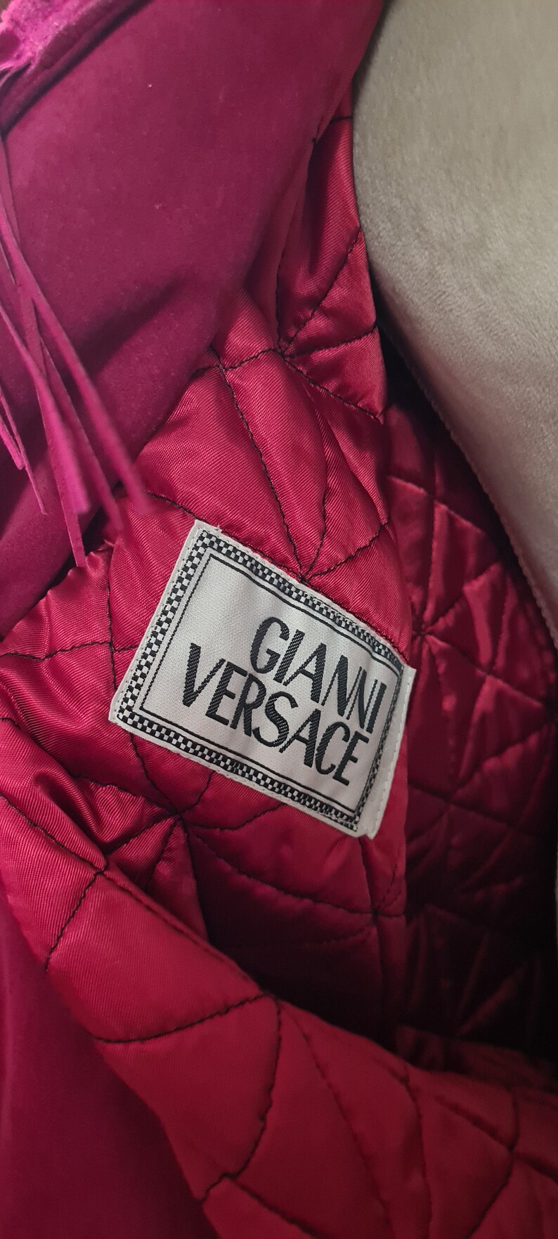 May include: A close-up of the inside of a pink jacket with a white label that reads "Gianni Versace".