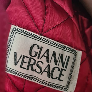 May include: A close-up of a red quilted fabric with a white label that reads "Gianni Versace".
