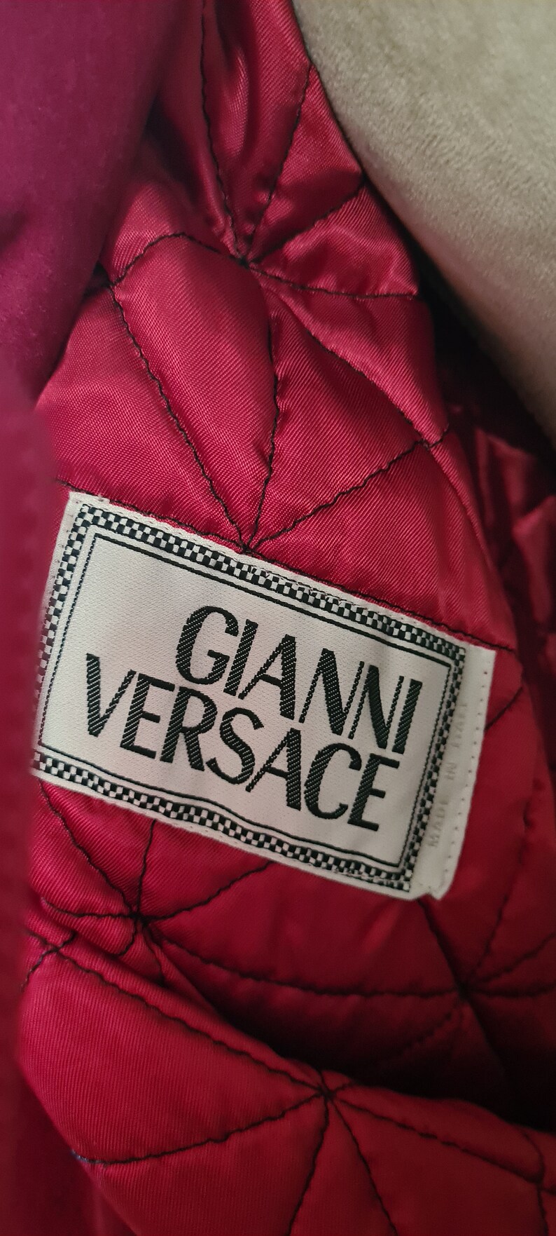 May include: A close-up of a red quilted fabric with a white label that reads "Gianni Versace".