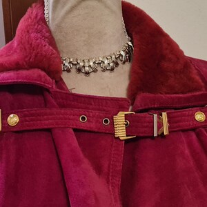 May include: A burgundy velvet jacket with a fur collar and gold buckles. The jacket has a long, flowing silhouette and is perfect for a wintery day.