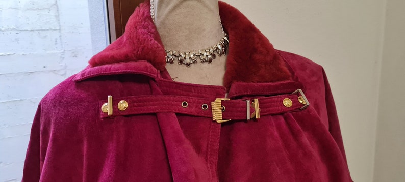 May include: A burgundy velvet jacket with a fur collar and gold buckles. The jacket has a long, flowing silhouette and is perfect for a wintery day.
