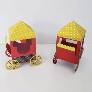 May include: Two red paper train carriages with yellow polka-dot roofs and yellow wheels. One carriage has a Mickey Mouse cutout. The carriages are on a white surface.