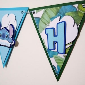 May include: A blue and green triangular banner with a cartoon character and the letter H. The character is blue with white eyes and is holding a sign that says "Aloha". The letter H is blue with a white outline.