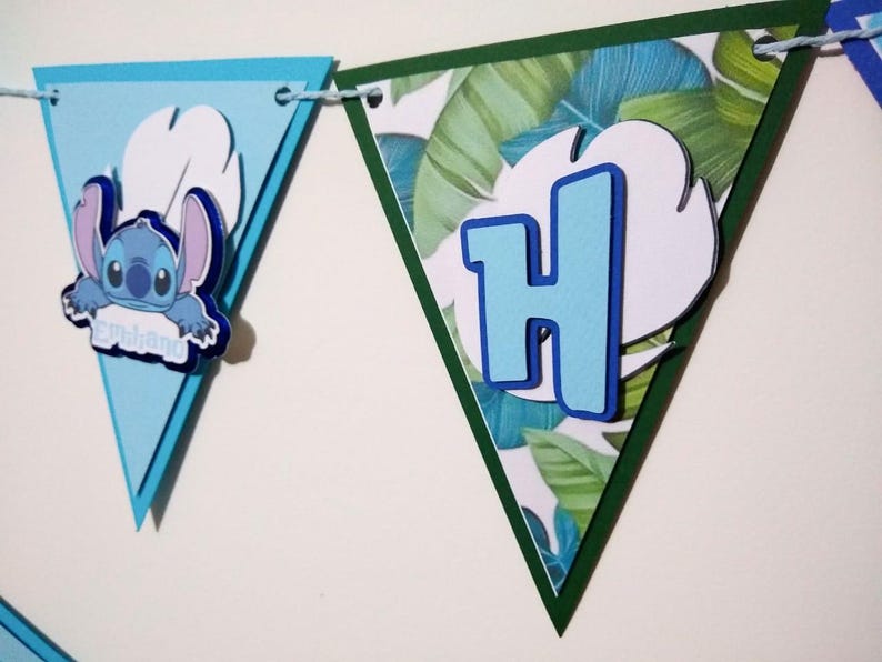 May include: A blue and green triangular banner with a cartoon character and the letter H. The character is blue with white eyes and is holding a sign that says "Aloha". The letter H is blue with a white outline.