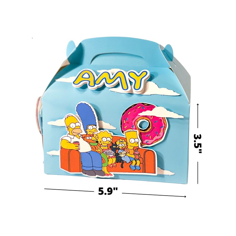 Puede incluir: Una caja de regalo de color azul y amarillo con tem&aacute;tica de Los Simpson con asa. La caja mide 5,9 pulgadas de ancho y 3,5 pulgadas de alto. La caja presenta a la familia Simpson sentada en un sof&aacute; con una dona en el fondo. El nombre "AMY" est&aacute; escrito en la parte delantera de la caja.
