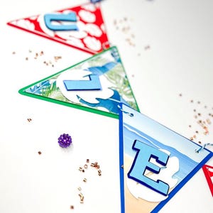 May include: A blue and white banner with the word "LOVE" spelled out in blue letters. The banner is decorated with tropical and beach themes. The banner is hanging from a string and there are purple and gold confetti scattered around it.