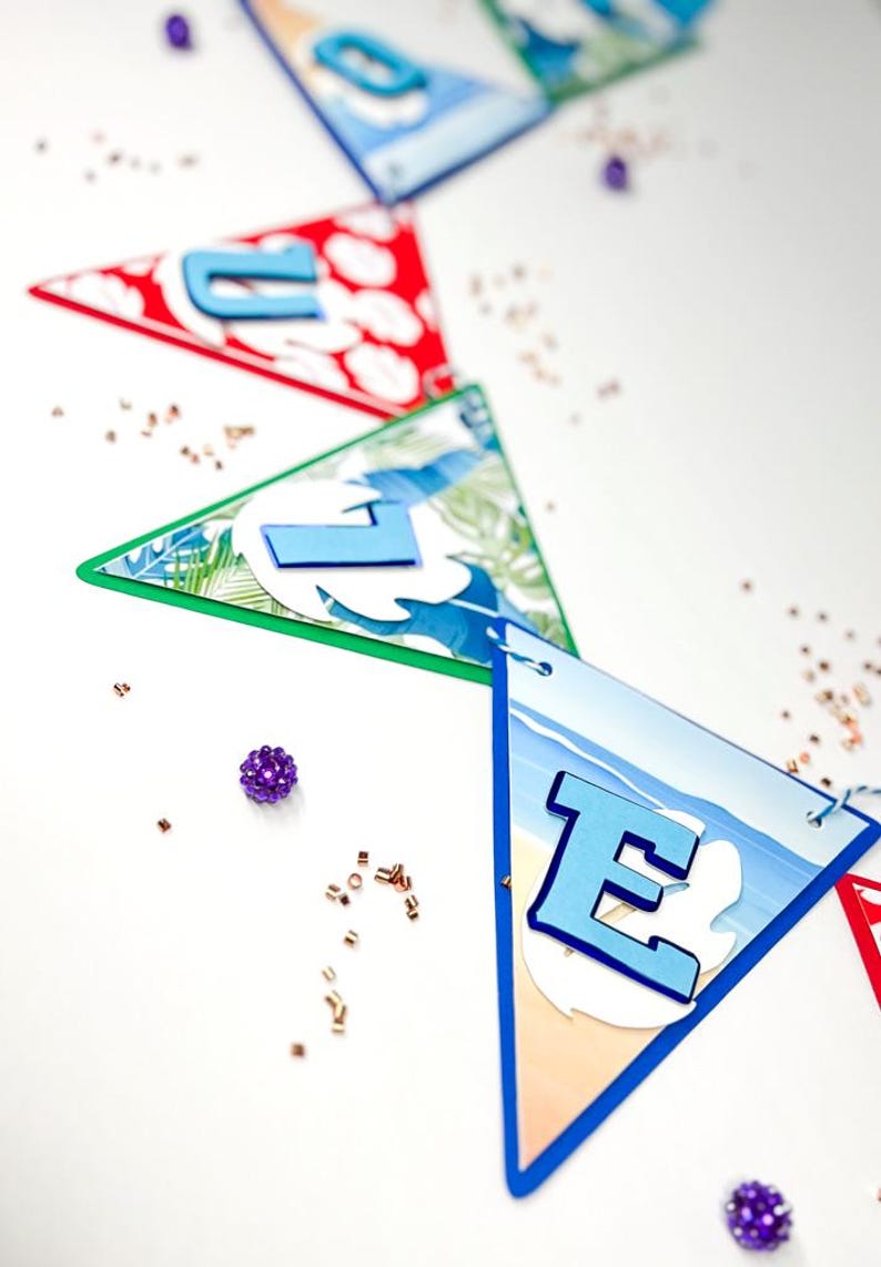 May include: A blue and white banner with the word "LOVE" spelled out in blue letters. The banner is decorated with tropical and beach themes. The banner is hanging from a string and there are purple and gold confetti scattered around it.