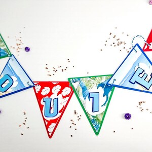 May include: A colorful paper banner with the word "OUTIE" spelled out in blue letters on triangular flags. Each flag has a different tropical design, including palm leaves, ocean waves, and flowers.