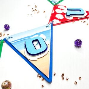 May include: A blue and white beach-themed banner with the number "0" in blue on a white background. The banner is made of paper and has a scalloped edge. The number is raised and has a white outline.