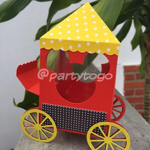 May include: A red and yellow paper train-shaped box with a Mickey Mouse head cutout. The train has yellow wheels, a yellow polka-dot roof, and a black and white dotted panel. The text "@partytogo" is visible on the side.
