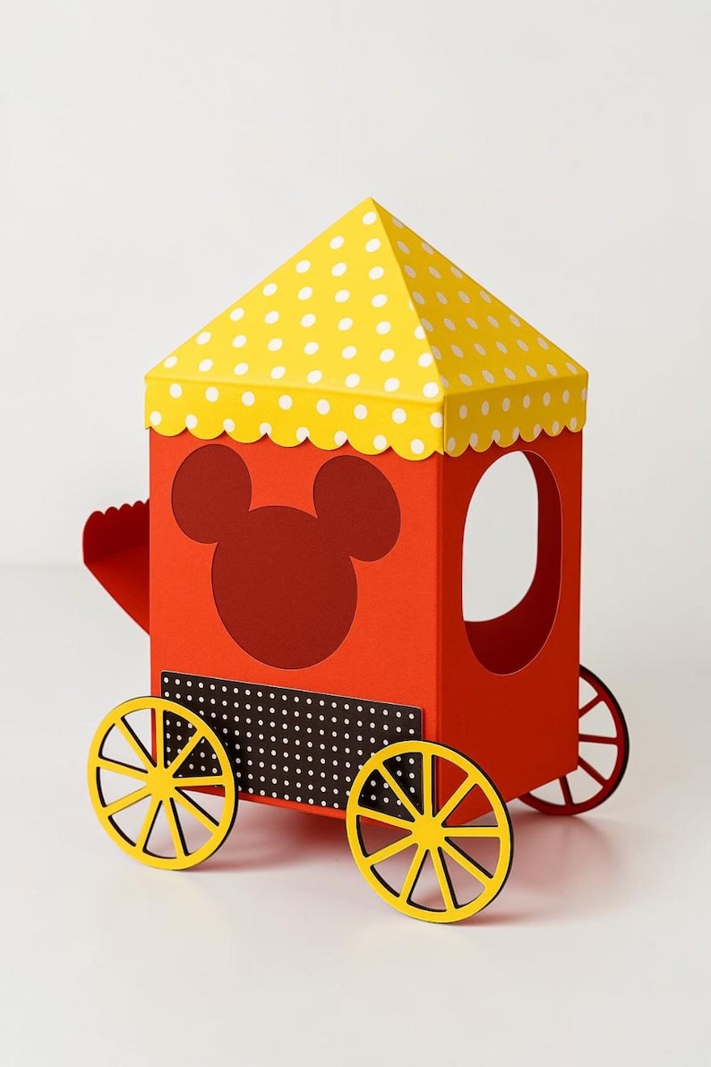May include: A red paper train car with a yellow polka-dot roof and yellow wheels. The train car features a Mickey Mouse silhouette and a black and white dotted panel. The wheels are yellow with black outlines.