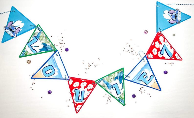 May include: A blue, green, and red triangular banner with the word "L-O-U-I-E" spelled out in blue letters. The banner is decorated with a cartoon character and a beach theme.