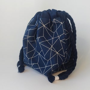Op de afbeelding: Een marineblauwe trekkoordtas met een wit geometrisch patroon. De tas heeft een dik, donkerblauw touw als trekkoord. Geschikt voor het dragen van kleine items.