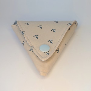 May include: A small, triangular beige fabric pouch with a blue anchor pattern and a light blue button closure.