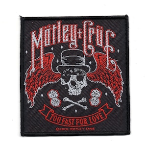 May include: Black square patch with a skull in a top hat, red wings, dice, and crossbones. The text "Mötley Crüe" is at the top, and "TOO FAST FOR LOVE" is on a banner below the skull. The patch is a rock band emblem.
