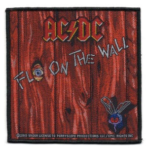 May include: Square patch featuring the AC/DC logo in red and yellow, and the words "FLO ON THE WALL" in white. The background is a red wood grain design with a cartoon fly. The patch has a black border.