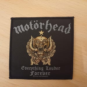 May include: Black embroidered patch with the text "Motörhead" in silver lettering. The patch features a gold skull with horns and wings, and the text "Everything Louder Forever" in silver lettering. ©2021 Motörhead.
