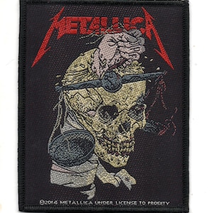 May include: Black embroidered patch with the word "METALLICA" in red lettering. The patch features a skull with a brain exposed and a bandage wrapped around its head. The text "©2014 METALLICA UNDER LICENSE TO PRODITY" is at the bottom of the patch.