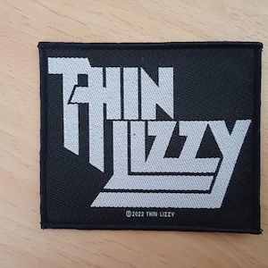 Op de afbeelding: Zwarte stoffen patch met witte tekst "Thin Lizzy" met een copyright symbool en het jaar 2022.