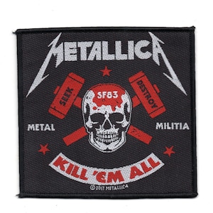 Op de afbeelding: Vierkant zwart embleem met de bandnaam "METALLICA" in wit, met een schedel en gekruiste hamers ontwerp. Het embleem bevat de tekst "SEEK", "DESTROY", "METAL", "MILITIA" en "KILL 'EM ALL". Rode sterren en tekst maken het ontwerp compleet.