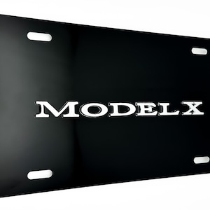 May include: A glossy black license plate with the word "MODEL X" in silver, centered on the plate. The plate has four mounting holes, one in each corner. The background is white.
