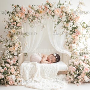 May include: A newborn baby sleeping on a white bed with a floral canopy. The canopy is made of pink and white flowers and greenery. The bed is decorated with a white blanket.