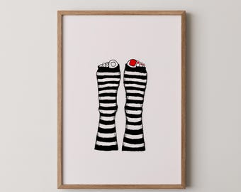 May include: A framed art print featuring a whimsical illustration of two feet wearing black and white striped socks. One foot has red nail polish. The artwork is set against a white background, framed in a light brown wooden frame.