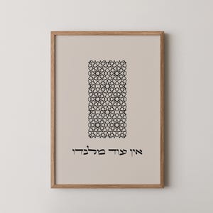 May include: Framed art print featuring a beige background with a black geometric pattern in the center. The text at the bottom is in Hebrew. The frame is made of light brown wood.