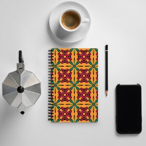 May include: A spiral bound notebook with a bright orange cover featuring a repeating pattern of pink and teal floral designs. The notebook is on a white surface with a coffee cup, pencil, and smartphone.