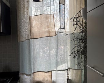 May include: A patchwork curtain hangs in front of a window, featuring a mix of fabrics in beige, blue, and white. The curtain is composed of rectangular and square patches, creating a unique, textured design. The window is letting in natural light.