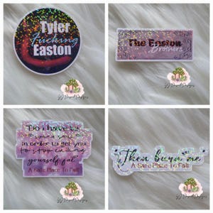 May include: Four holographic stickers with text. One sticker reads "Tyler Fucking Easton" in blue and white on a dark background. Another says "The Easton Brothers" in purple. The other two stickers have quotes from "A Safe Place To Fall".