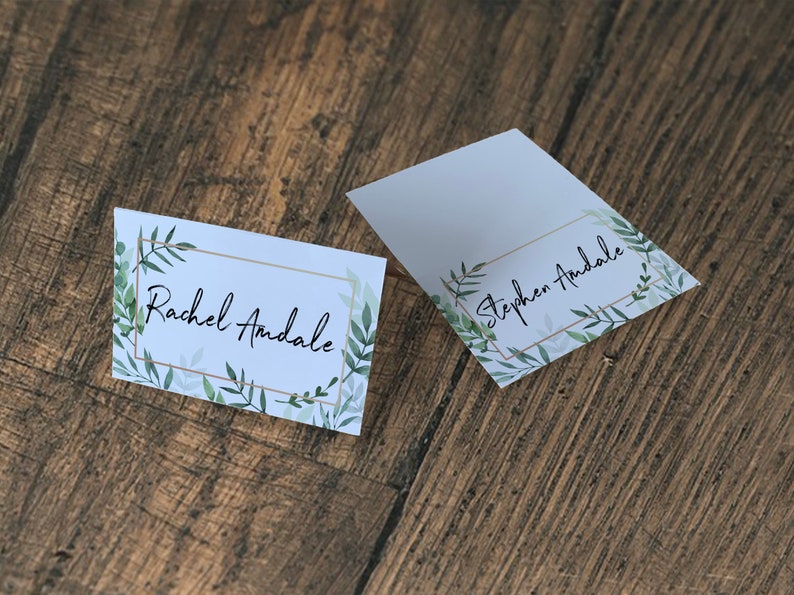 May include: Two white place cards with gold frames and green watercolor leaves. The text on the cards reads "Rachel Andale" and "Stephen Andale".