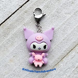May include: A purple and white character with pig ears and a pink piglet in its arms. The character is attached to a silver charm loop. The character is a popular Japanese cartoon character.